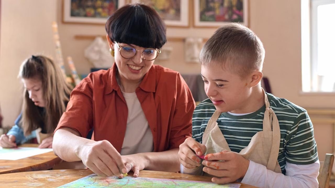 A support worker helping a young participant with a creative art activity