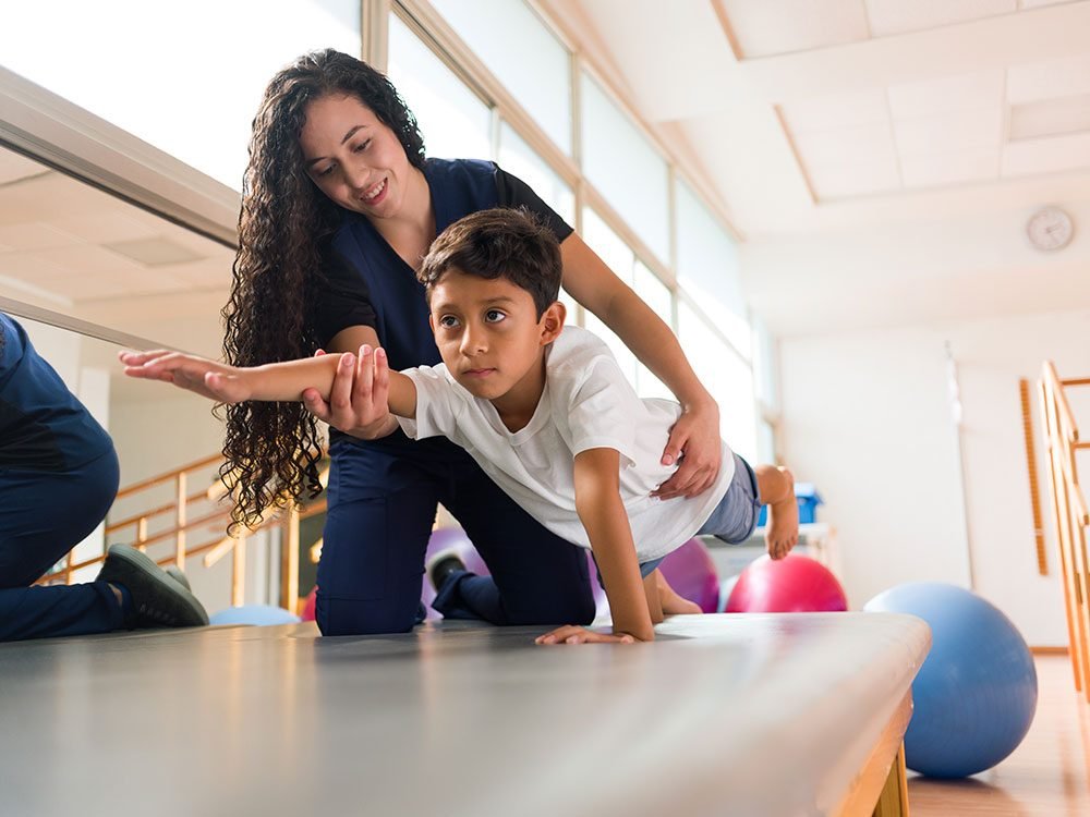 A therapist supporting a young boy through a physical therapy exercise